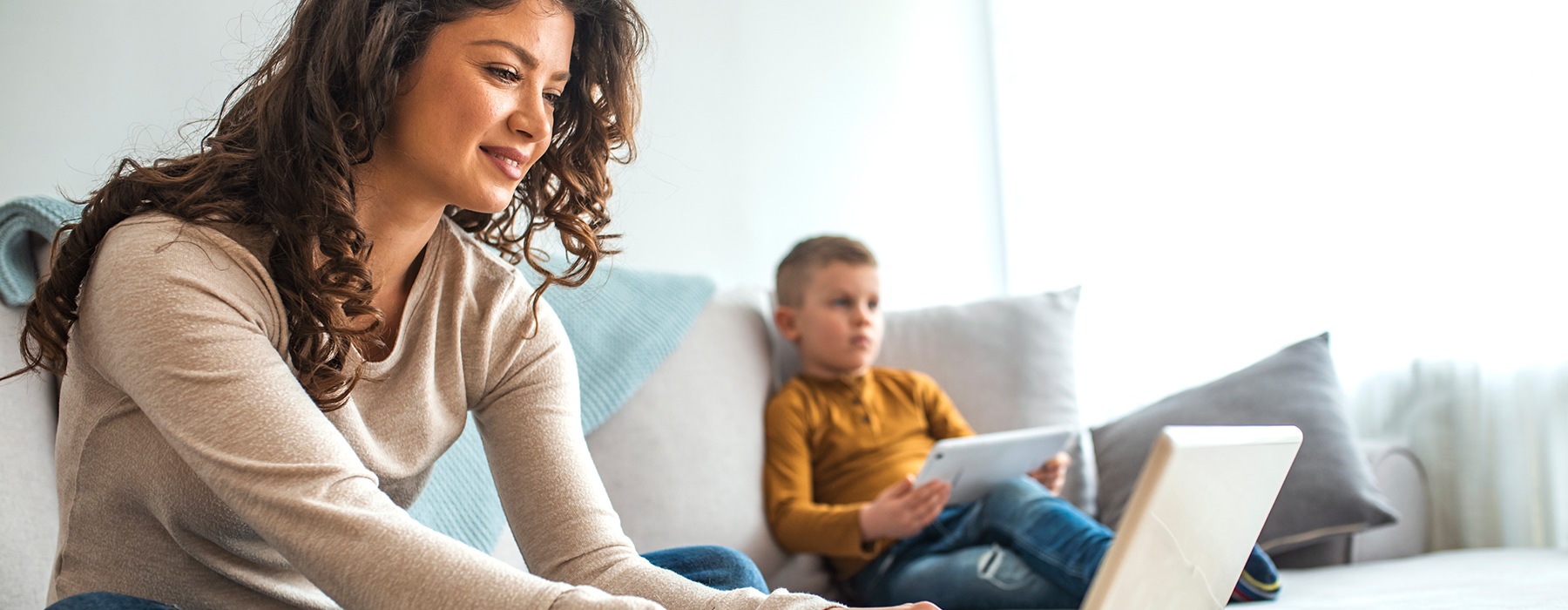 A mom is working on her computer with her son nearby 